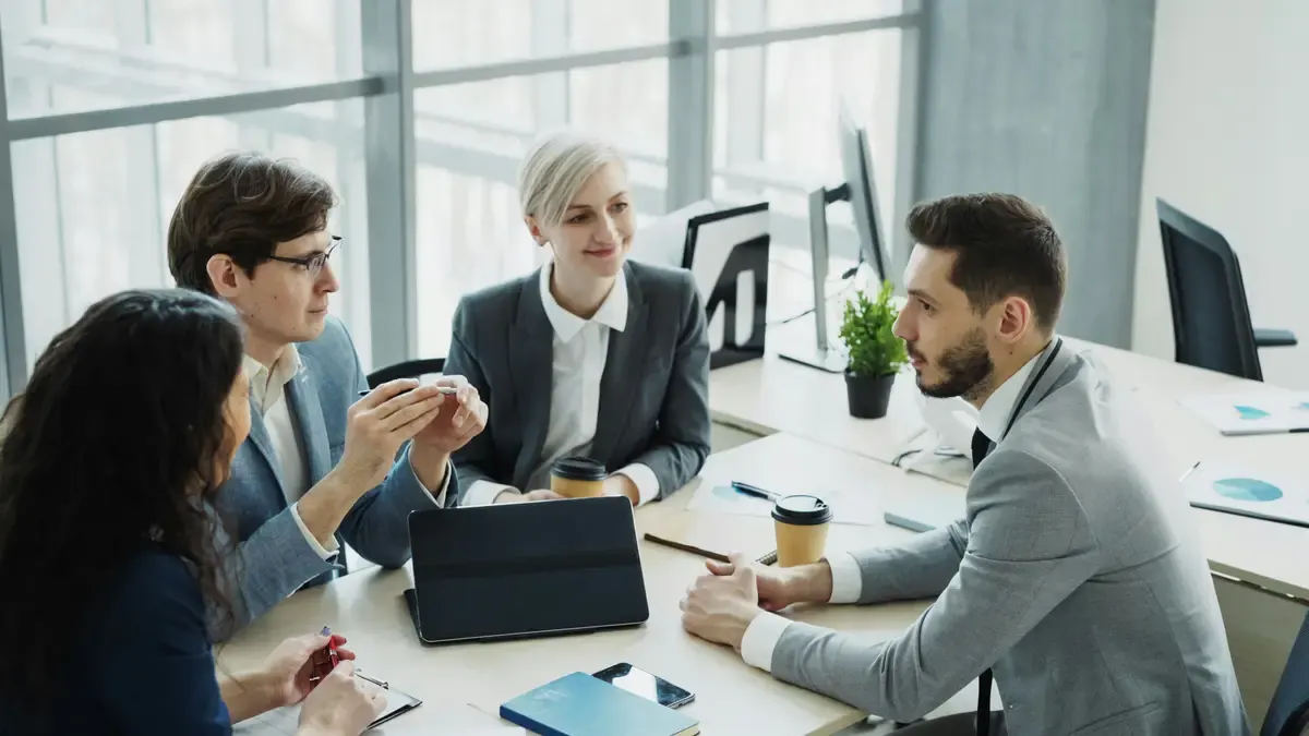 Four colleagues in discussion around an office table with a tablet and coffee cups