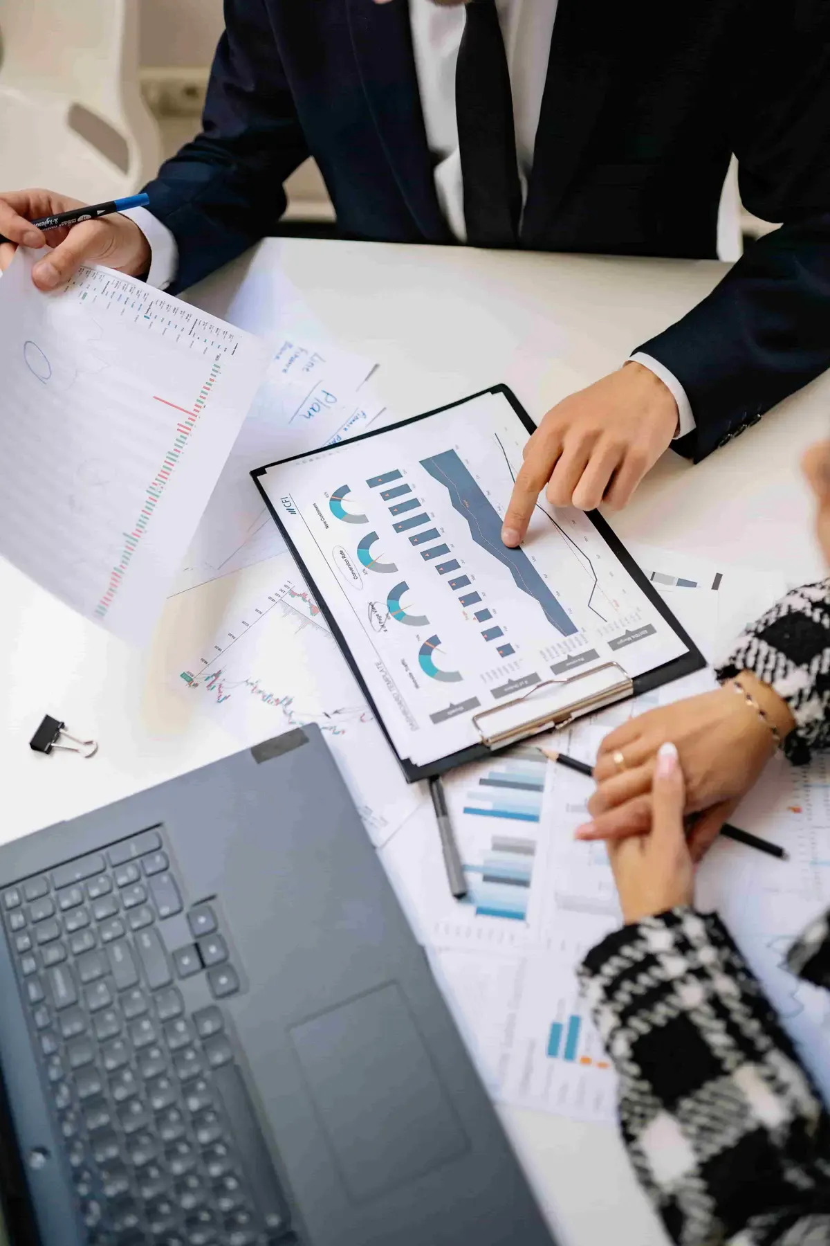 Two colleagues reviewing printed business charts on a clipboard beside a laptop