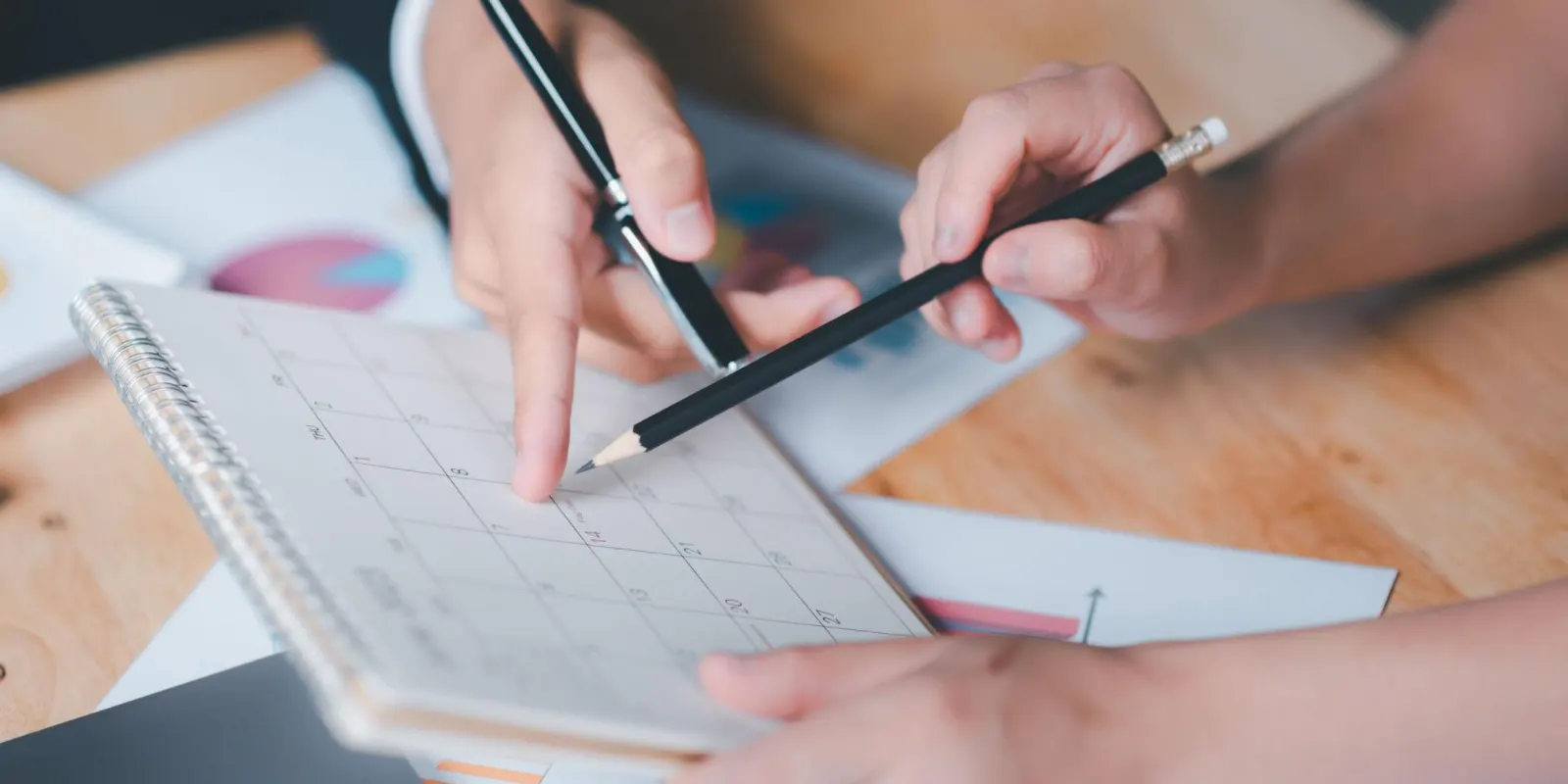 Two people marking dates on a desk calendar beside printed charts