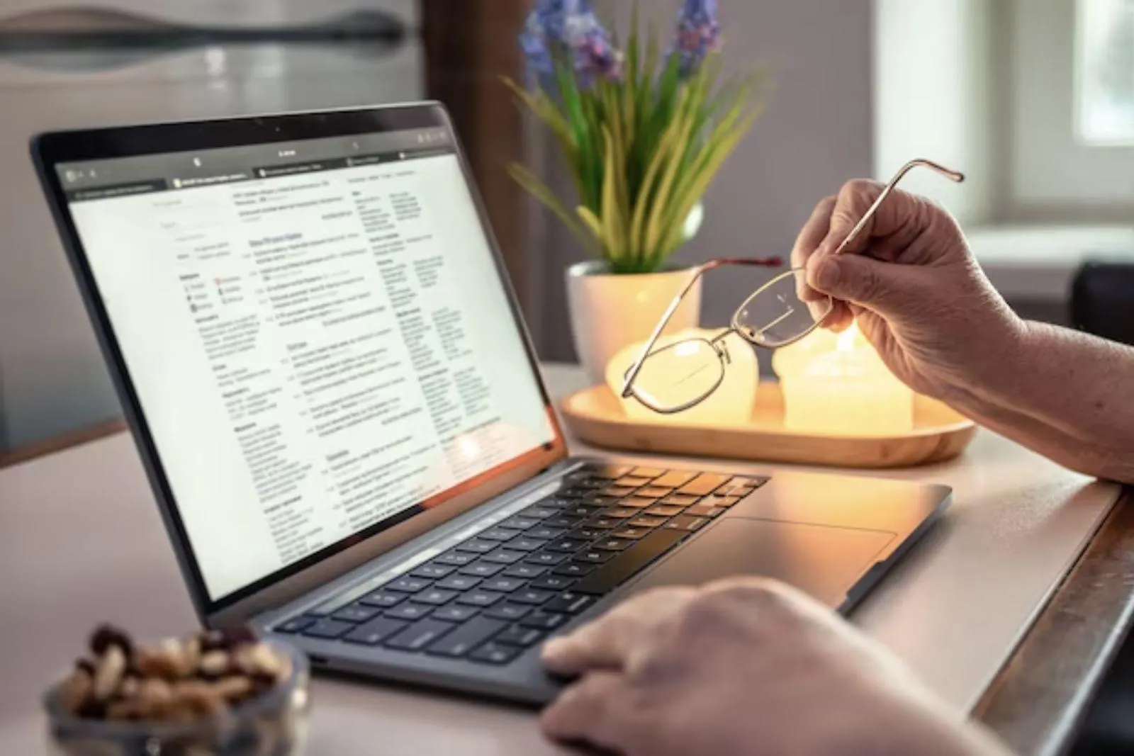 A person holding reading glasses while reading a document on a laptop