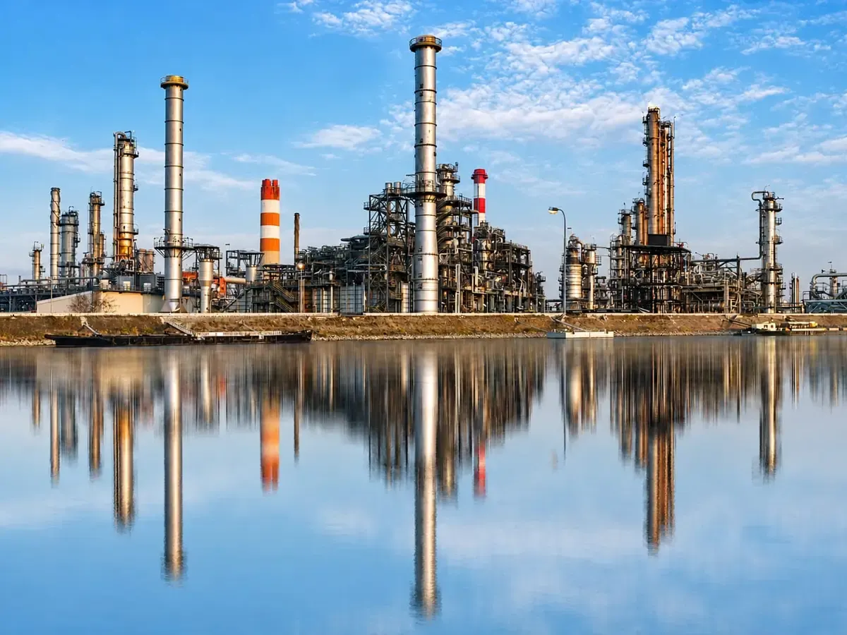 An industrial plant reflected in still water under a blue sky