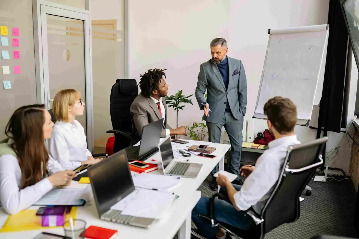 A presenter at a flip chart leading a discussion with colleagues around a meeting table