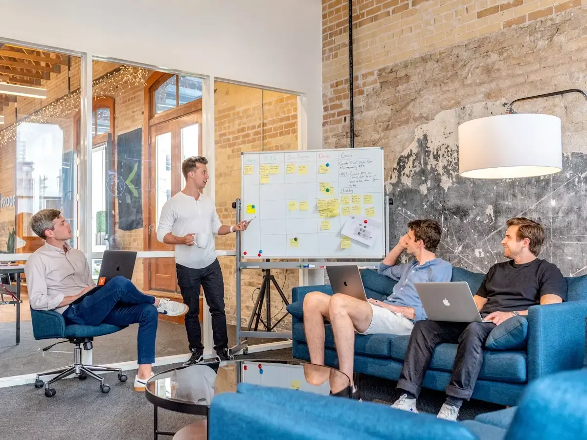 A team member presenting a whiteboard of sticky notes to three colleagues with laptops